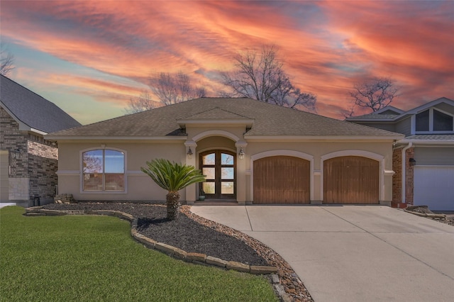 view of front facade with a garage, driveway, a lawn, roof with shingles, and stucco siding