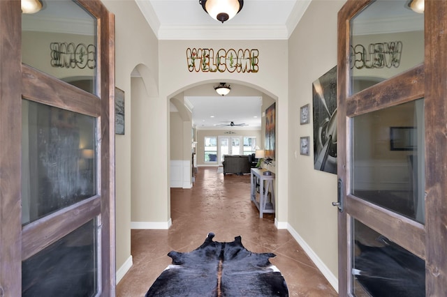 foyer featuring baseboards, ceiling fan, arched walkways, and crown molding