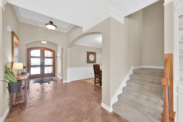 entrance foyer with arched walkways, a decorative wall, french doors, wainscoting, and crown molding