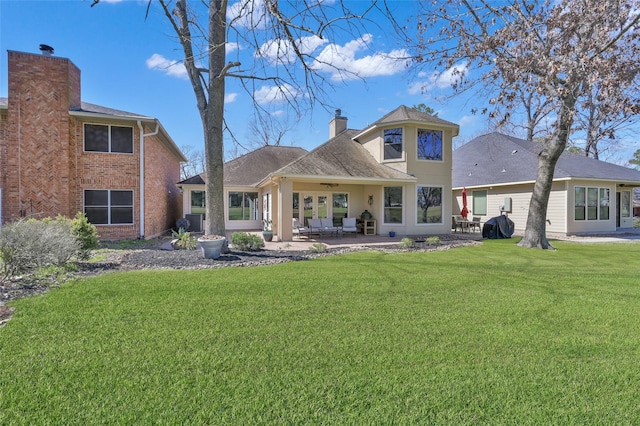 back of property with stucco siding, a patio, a chimney, and a lawn