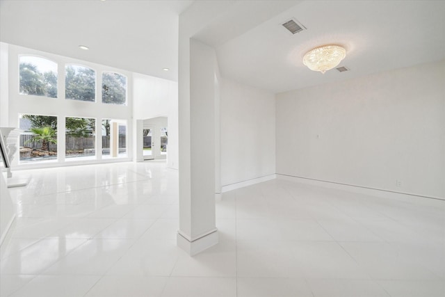 spare room featuring visible vents, a towering ceiling, baseboards, and light tile patterned floors