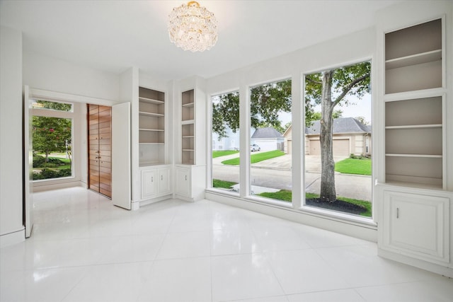 unfurnished room with built in shelves, an inviting chandelier, and light tile patterned floors