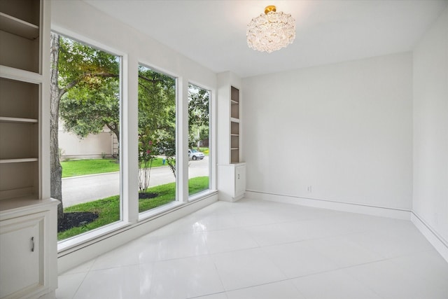 unfurnished room with light tile patterned floors, built in shelves, a chandelier, and baseboards