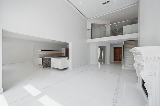 unfurnished living room with a fireplace, light tile patterned floors, visible vents, stairway, and a towering ceiling