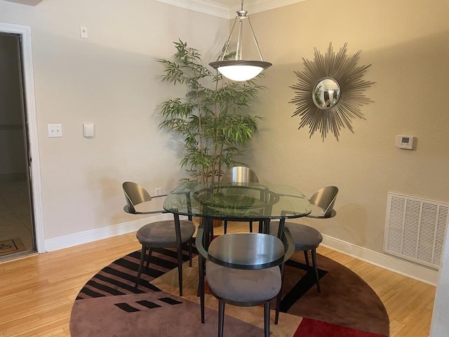 dining area with ornamental molding, light wood-type flooring, visible vents, and baseboards