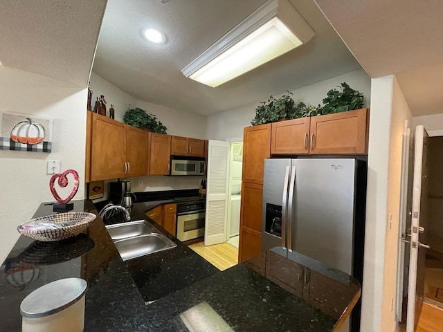 kitchen with a peninsula, appliances with stainless steel finishes, a sink, and brown cabinets