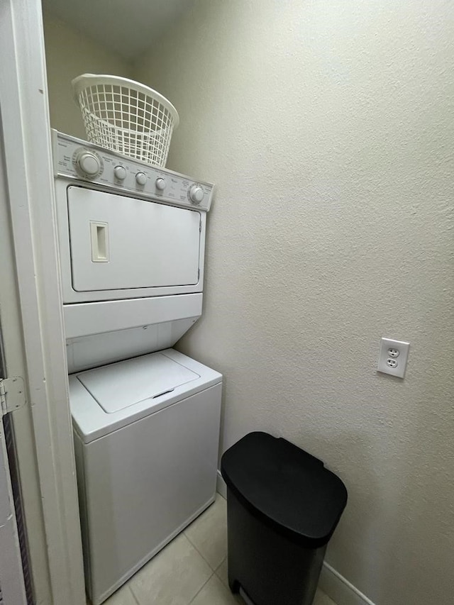 clothes washing area with light tile patterned floors, laundry area, a textured wall, and stacked washer and clothes dryer