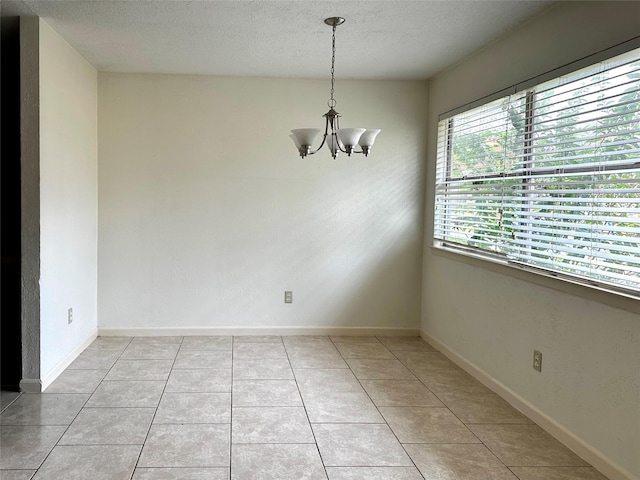 unfurnished dining area featuring light tile patterned floors, a textured ceiling, baseboards, and a notable chandelier