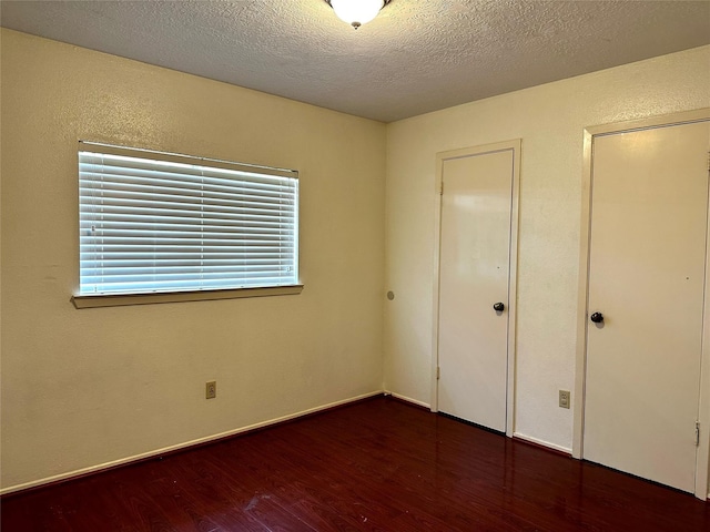 unfurnished bedroom with a textured wall, dark wood finished floors, a textured ceiling, and baseboards