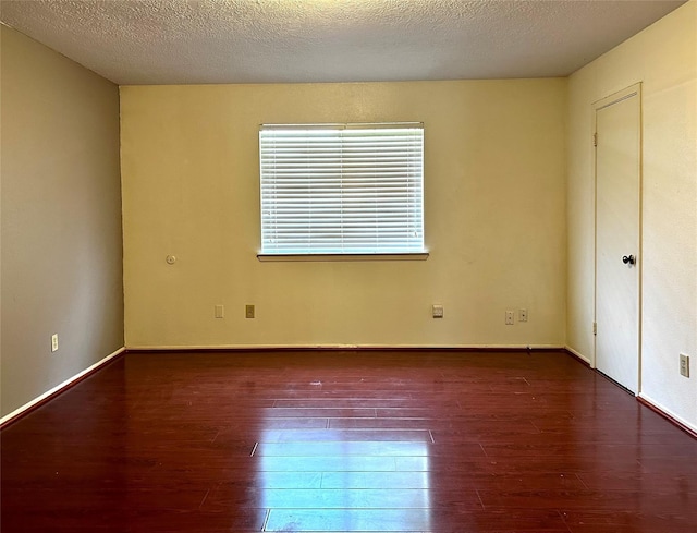 spare room with dark wood finished floors, a textured ceiling, and baseboards