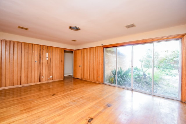 spare room featuring light wood-style floors, wooden walls, and visible vents