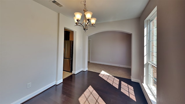 spare room featuring arched walkways, visible vents, an inviting chandelier, wood finished floors, and baseboards