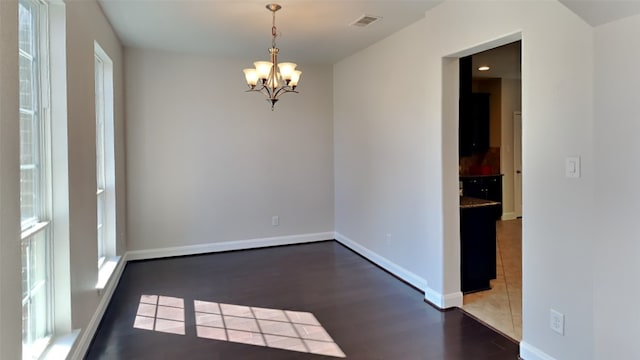 unfurnished room featuring a chandelier, visible vents, baseboards, and wood finished floors