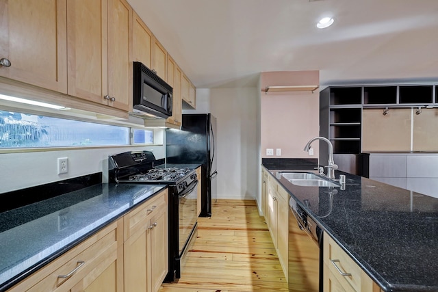 kitchen featuring light wood-style flooring, light brown cabinets, a sink, dark stone counters, and black appliances