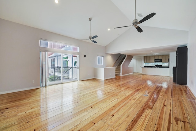 unfurnished living room with light wood finished floors, baseboards, ceiling fan, stairs, and high vaulted ceiling