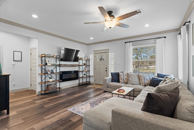 living room with dark wood-style flooring, a glass covered fireplace, visible vents, and crown molding