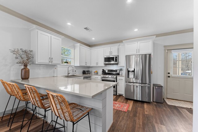 kitchen featuring a breakfast bar, light countertops, appliances with stainless steel finishes, white cabinets, and a sink