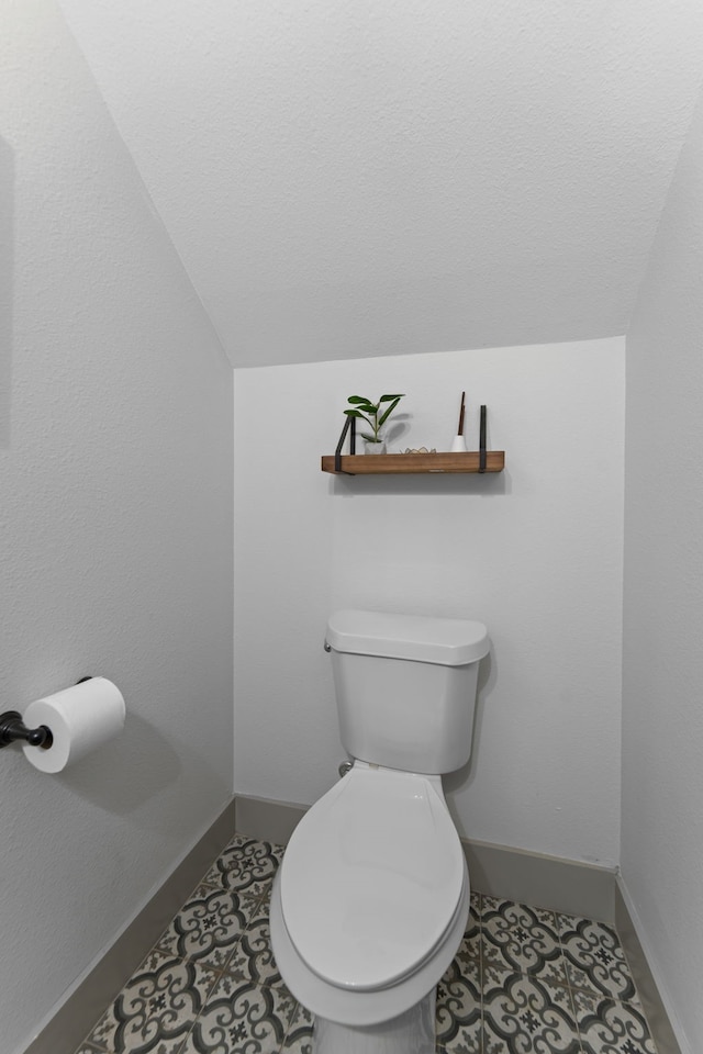 bathroom with toilet, vaulted ceiling, a textured ceiling, baseboards, and tile patterned floors