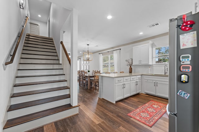 kitchen with pendant lighting, light countertops, freestanding refrigerator, white cabinetry, and a peninsula