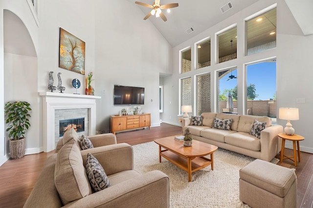 living area with a tiled fireplace, wood finished floors, visible vents, and a ceiling fan