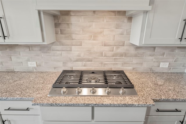 interior details featuring light stone counters, stainless steel gas cooktop, white cabinets, and decorative backsplash