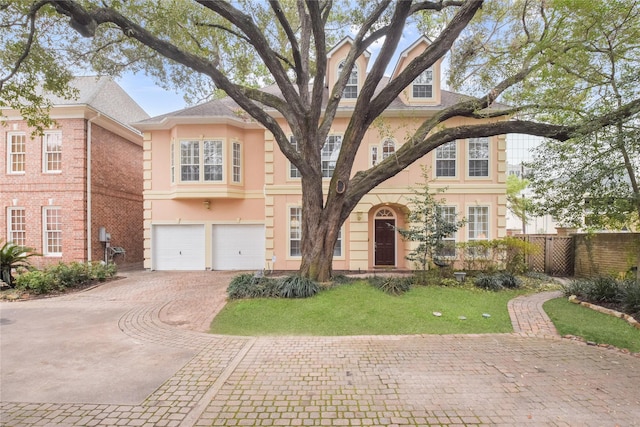 view of front of home with an attached garage, fence, driveway, stucco siding, and a front lawn