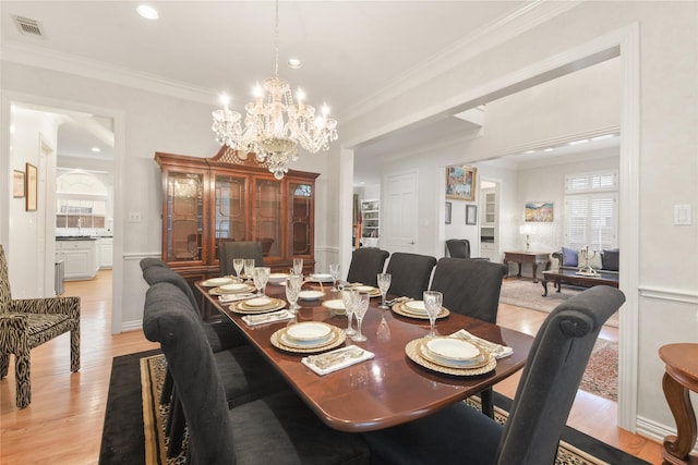 dining area with a notable chandelier, a wainscoted wall, visible vents, ornamental molding, and light wood-type flooring