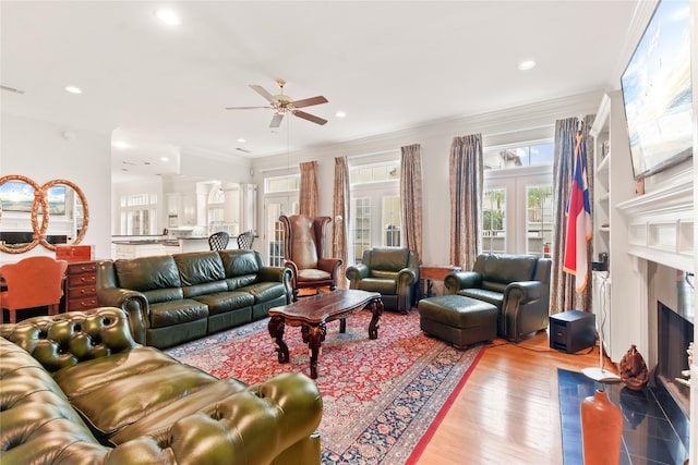 living area with crown molding, recessed lighting, light wood-style flooring, a ceiling fan, and a high end fireplace