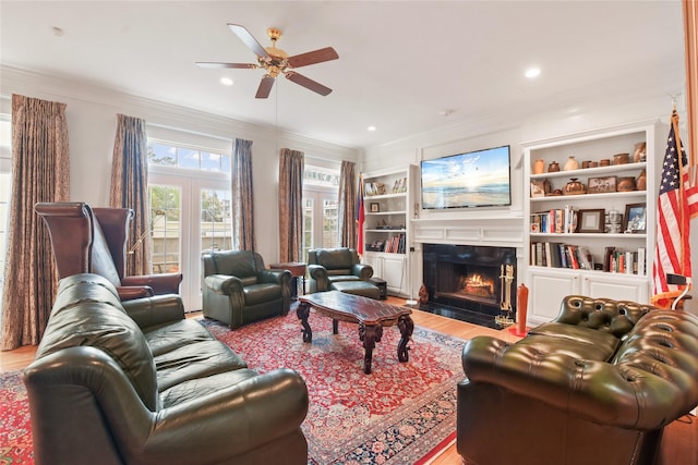 living area with a fireplace with flush hearth, ceiling fan, crown molding, and wood finished floors