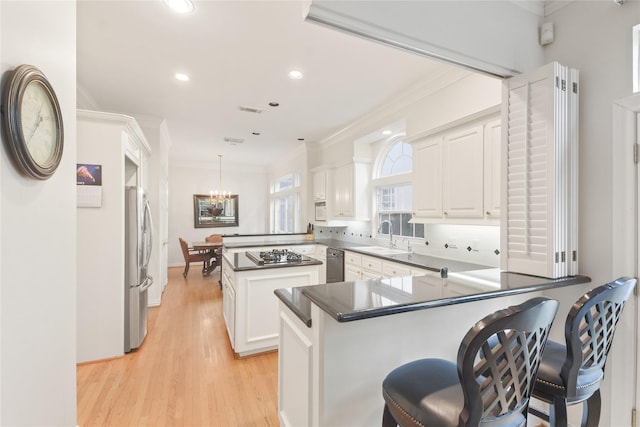 kitchen with a peninsula, hanging light fixtures, dark countertops, and white cabinetry