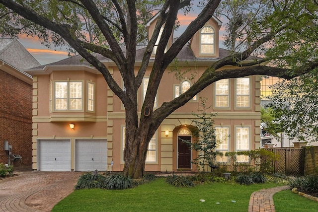 view of front facade with a yard, decorative driveway, an attached garage, and stucco siding