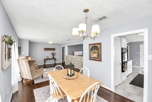 dining space with a textured ceiling, light wood finished floors, a chandelier, and visible vents