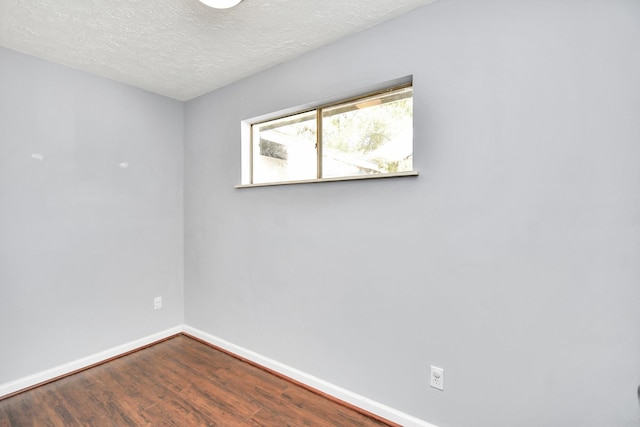 unfurnished room with a textured ceiling, baseboards, and wood finished floors