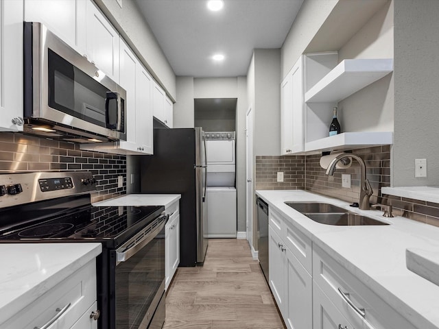 kitchen featuring open shelves, appliances with stainless steel finishes, stacked washer / dryer, white cabinetry, and a sink