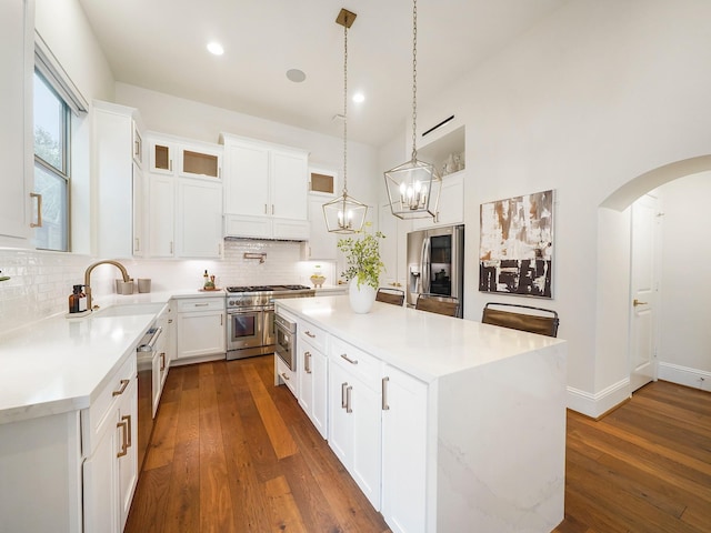 kitchen with dark wood-style floors, arched walkways, a sink, appliances with stainless steel finishes, and backsplash