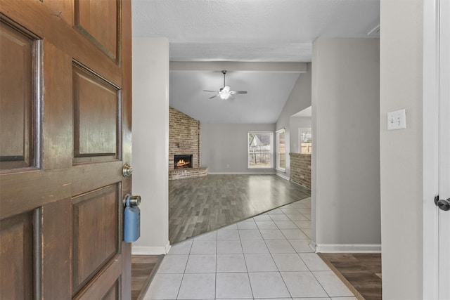 foyer with a fireplace, vaulted ceiling with beams, light tile patterned floors, a ceiling fan, and a textured ceiling