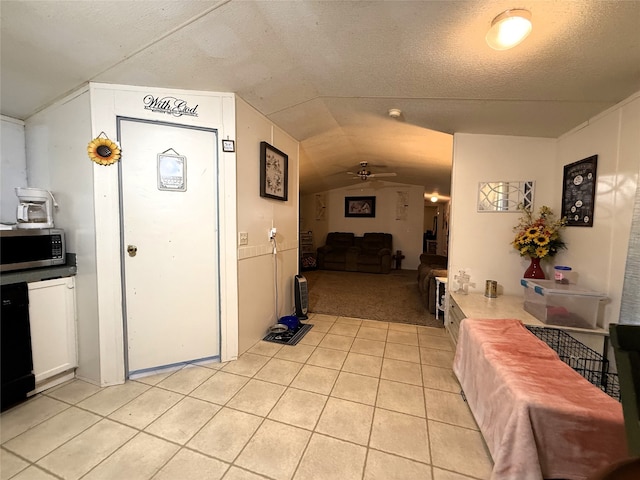 kitchen featuring light tile patterned floors, stainless steel microwave, vaulted ceiling, ceiling fan, and a textured ceiling