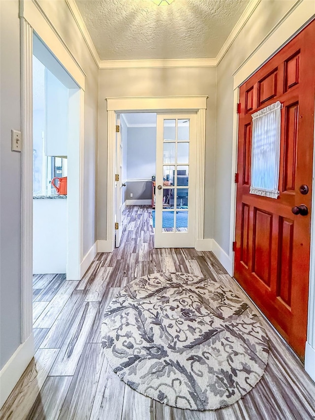 foyer with baseboards, ornamental molding, a textured ceiling, french doors, and light wood-type flooring