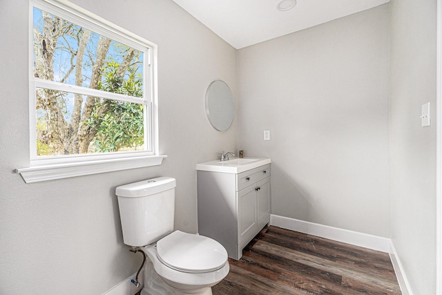 half bath with baseboards, vanity, toilet, and wood finished floors