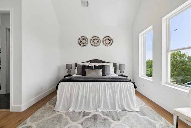 bedroom with baseboards, visible vents, vaulted ceiling, and wood finished floors