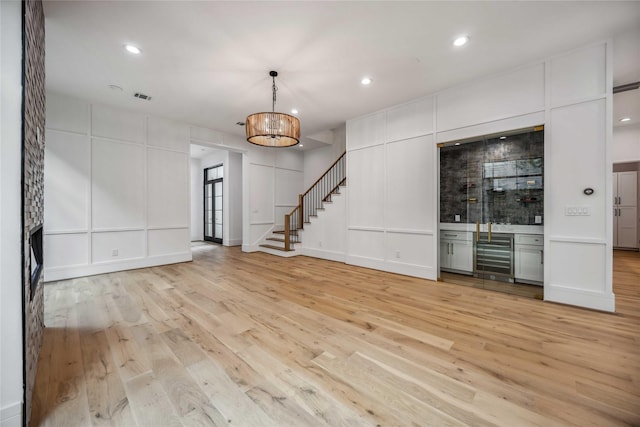 unfurnished room with light wood finished floors, stairway, visible vents, and a decorative wall