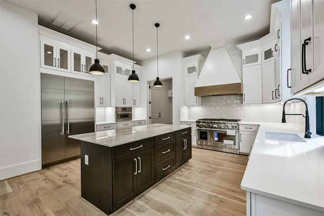 kitchen featuring a center island, high end appliances, glass insert cabinets, a sink, and premium range hood