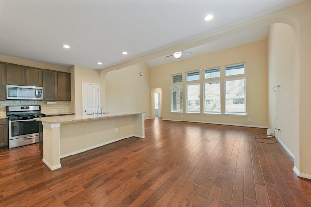 kitchen featuring a center island with sink, arched walkways, open floor plan, light stone countertops, and stainless steel appliances