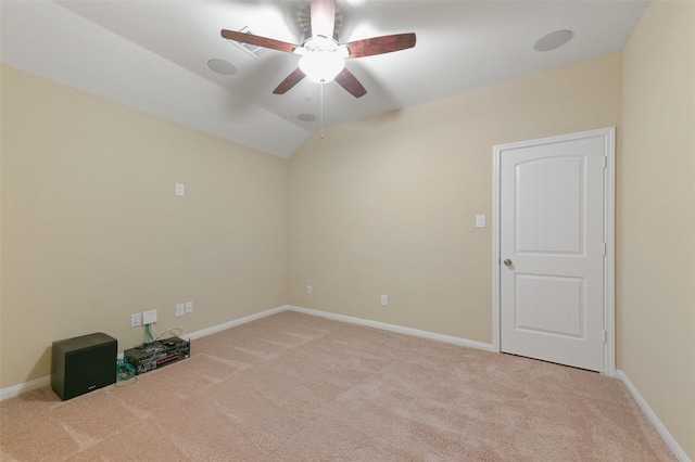 empty room with a ceiling fan, light colored carpet, vaulted ceiling, and baseboards