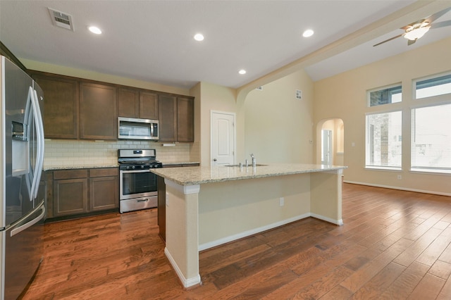 kitchen featuring light stone counters, visible vents, backsplash, appliances with stainless steel finishes, and a kitchen island with sink