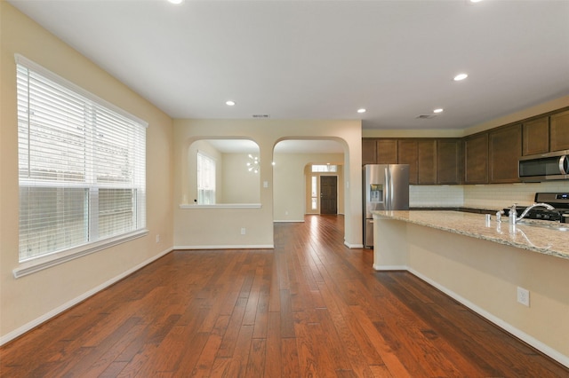 kitchen featuring light stone counters, decorative backsplash, appliances with stainless steel finishes, dark wood-type flooring, and a sink