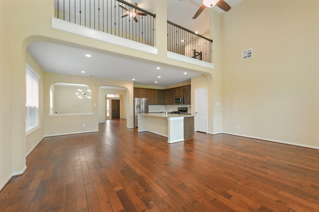 unfurnished living room featuring arched walkways, ceiling fan, dark wood-type flooring, visible vents, and baseboards