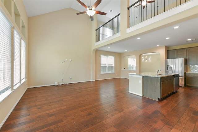 kitchen featuring dark wood-style flooring, open floor plan, a healthy amount of sunlight, an island with sink, and light stone countertops