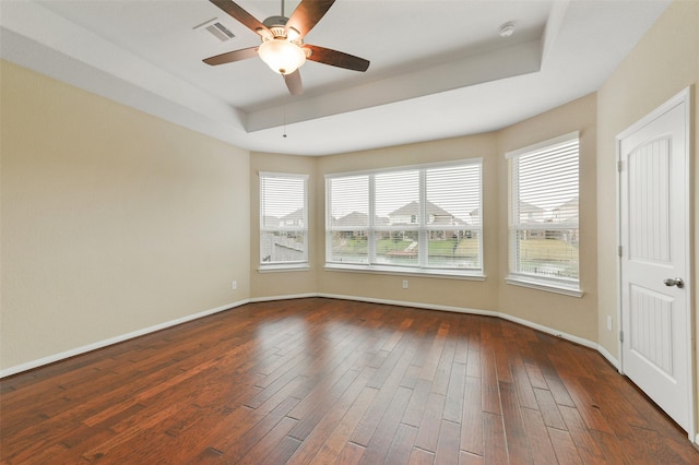 empty room featuring dark wood-style floors, a tray ceiling, visible vents, and baseboards