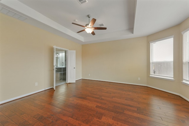 spare room featuring ceiling fan, visible vents, baseboards, a tray ceiling, and dark wood finished floors